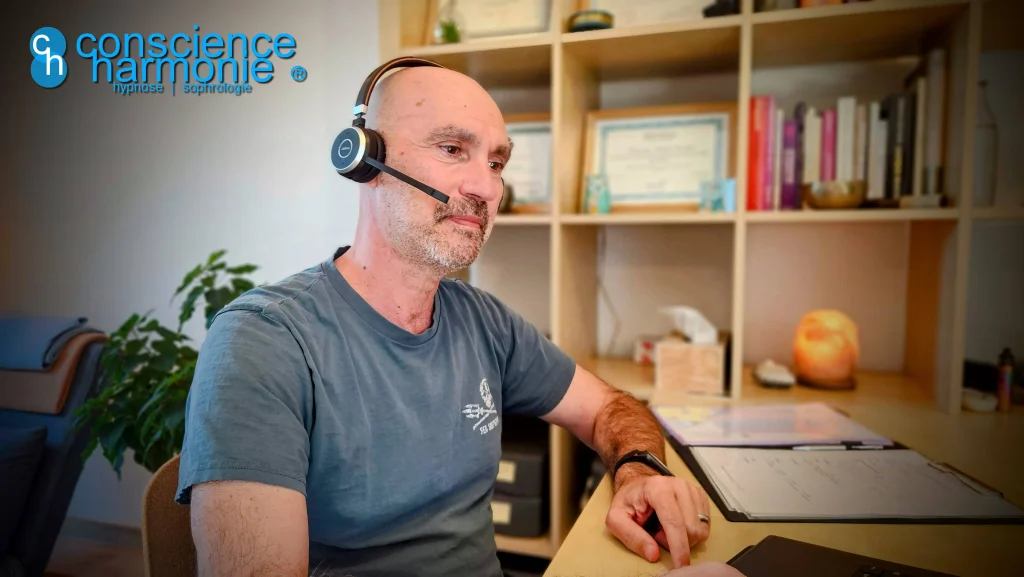 Portrait de Fabien Claudel Marion, praticien en hypnose, assis à son bureau en séance de consultation en ligne, portant un casque audio et souriant avec bienveillance.